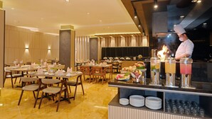 A modern restaurant with a chef preparing food, a buffet with various dishes, and a bar area with drinks. - Swiss-Belcourt Makassar (Makassar)