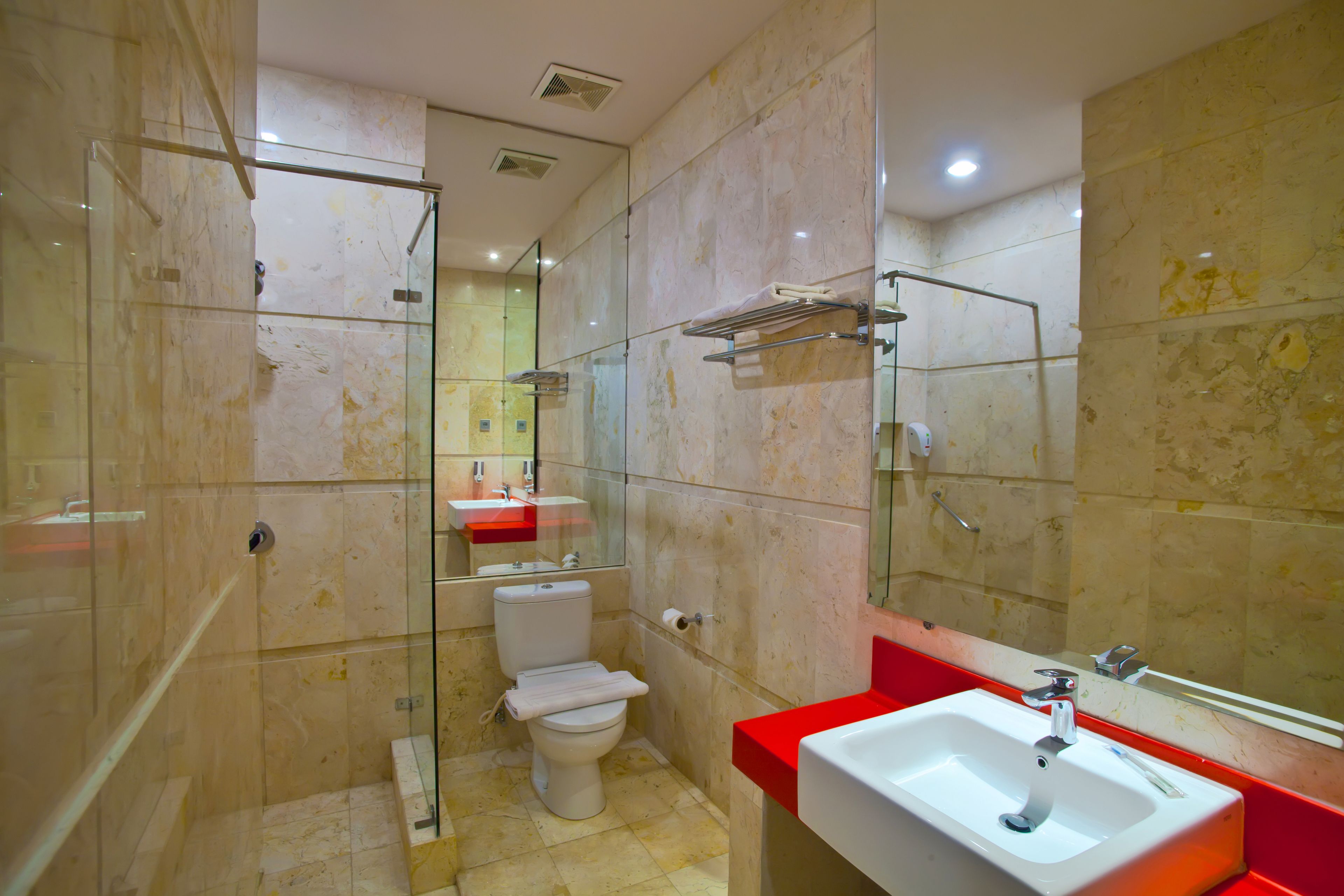 A modern bathroom with a glass shower enclosure, a white toilet, and a red sink.