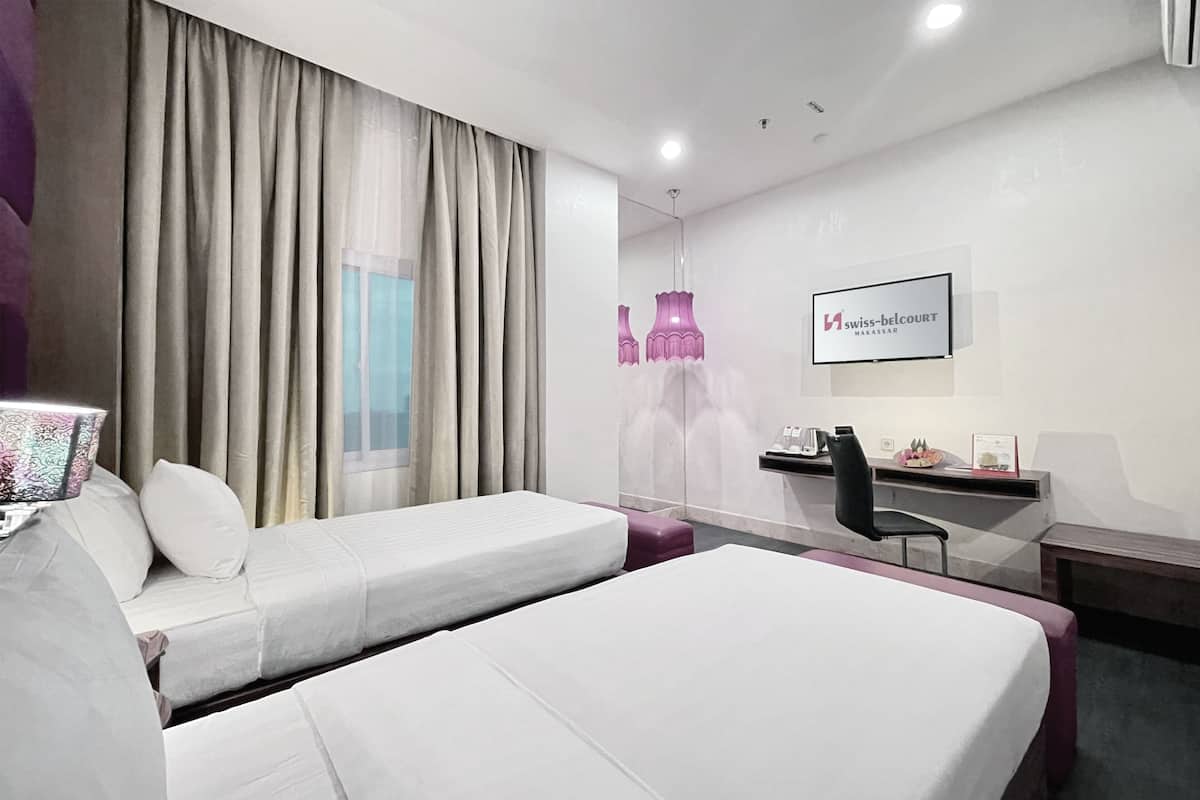 Habitación de hotel con dos camas, un escritorio, una silla y un amplio ventanal con cortinas.