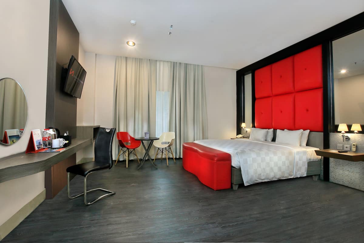 Una habitación de hotel moderna con una cama grande, un escritorio con una silla, un televisor y una pared de acento roja.