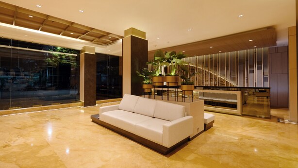 A spacious lobby with a white sofa, a staircase, and a large window overlooking a cityscape. - Swiss-Belcourt Makassar (Makassar)