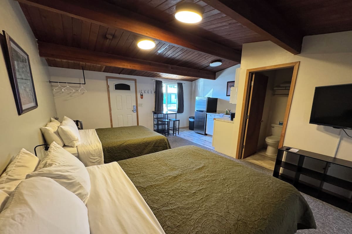 A room with two beds, a kitchenette, a TV, and a door leading to a bathroom.