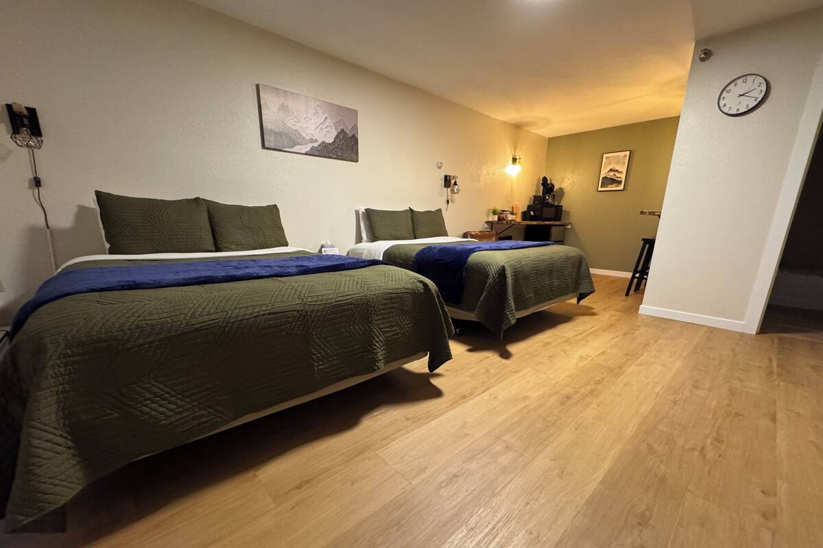 A bedroom with two beds, wooden flooring, a wall clock, and a painting.