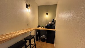 A compact kitchen with a wooden countertop, a black refrigerator, a coffee maker, and a trash bin. - The Pioneer Motel (Palmer)