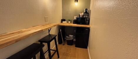 A compact kitchen with a wooden countertop, a black refrigerator, a coffee maker, and a trash bin.