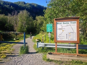 A West Butt Trail sign with a map and a person walking on a gravel path.