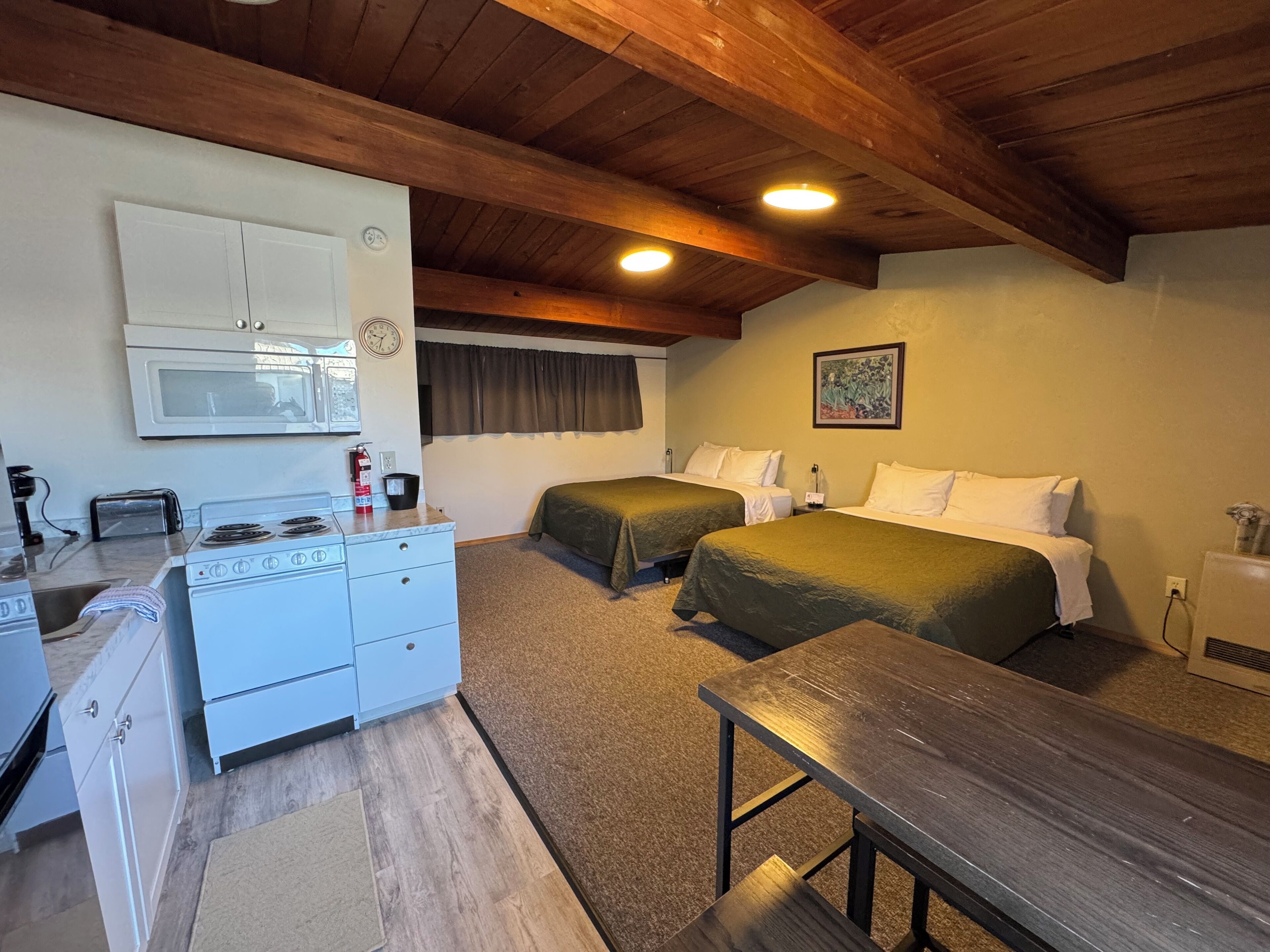 Una habitación pequeña con kitchenette, dos camas, techo de madera y un cuadro en la pared.