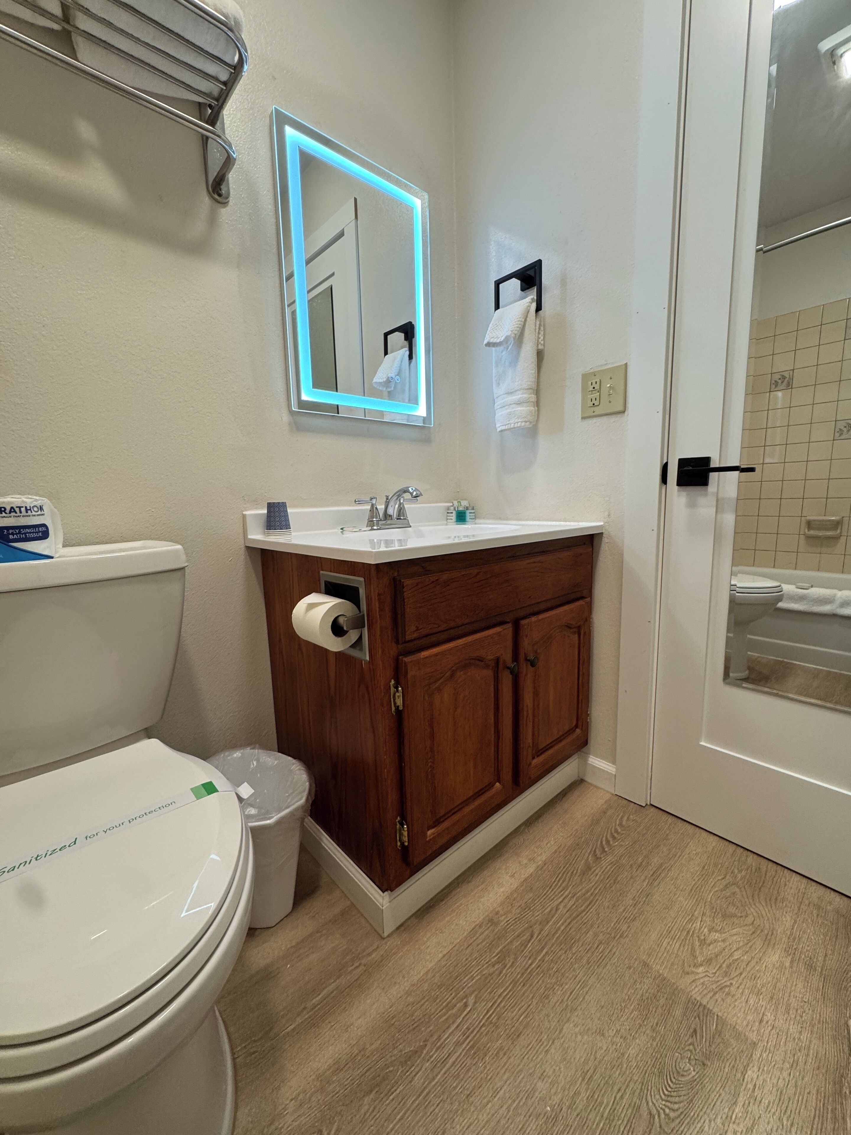 Et badeværelse med toilet, vask, kommode og et spejl med LED-belysning.