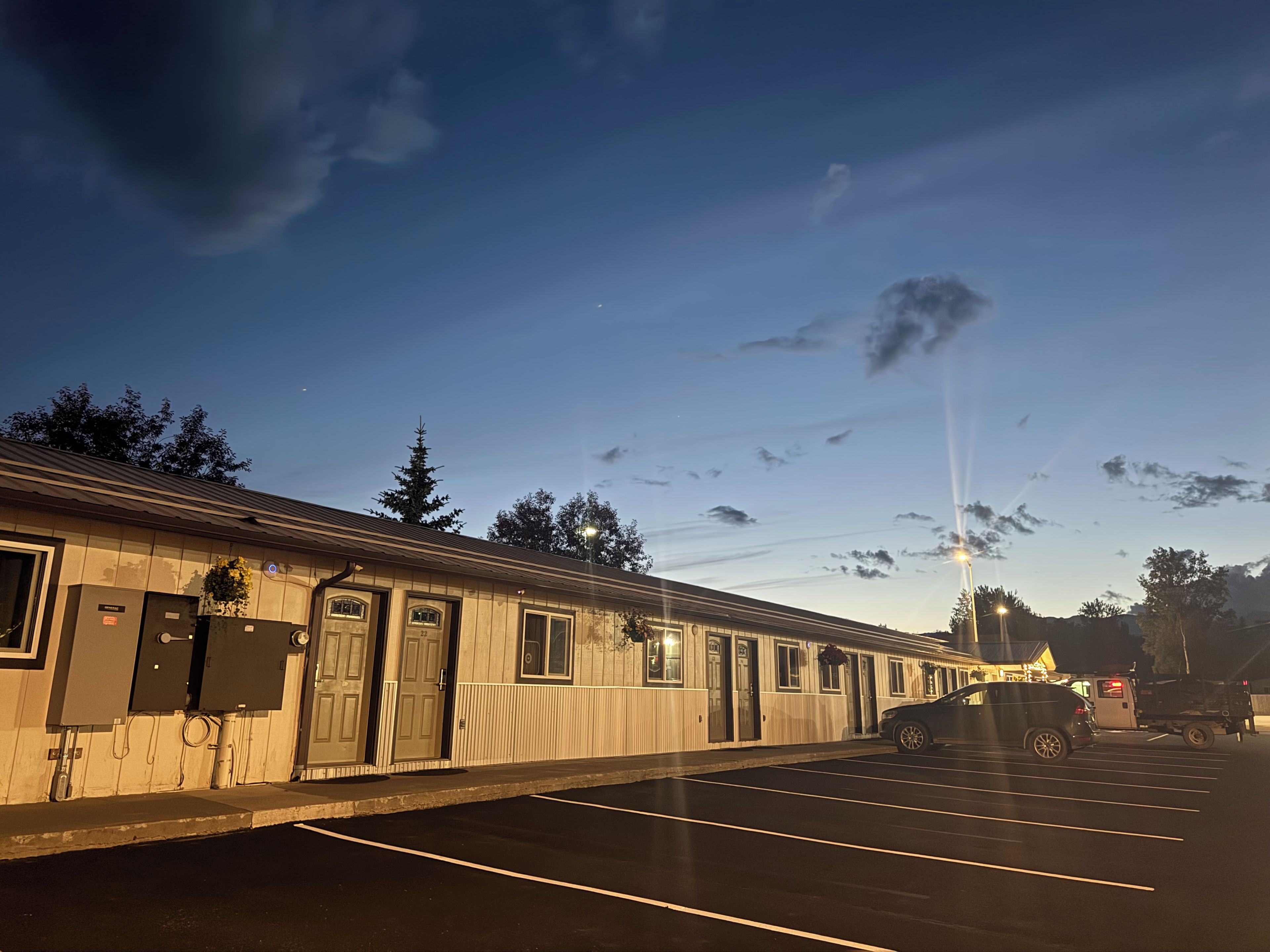 A motel with a row of rooms, a parking lot, and a clear sky.