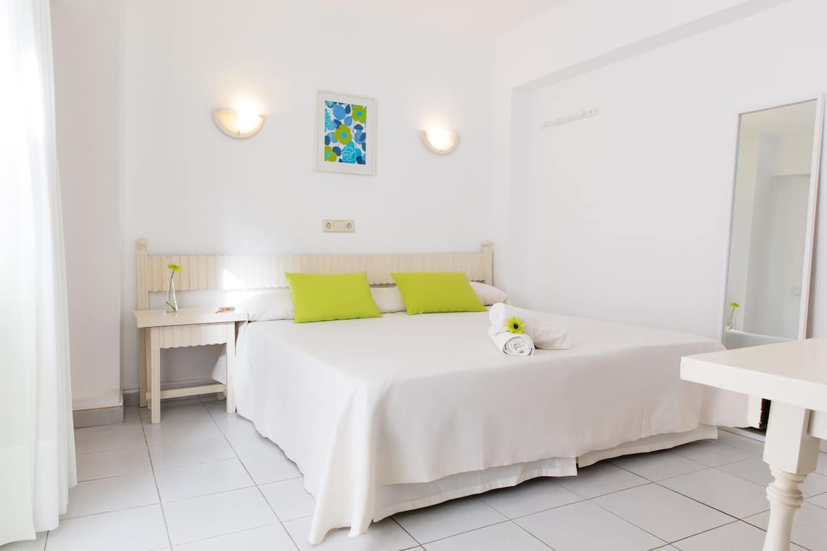 A clean, white bedroom with a bed, bedside table, and a mirror.