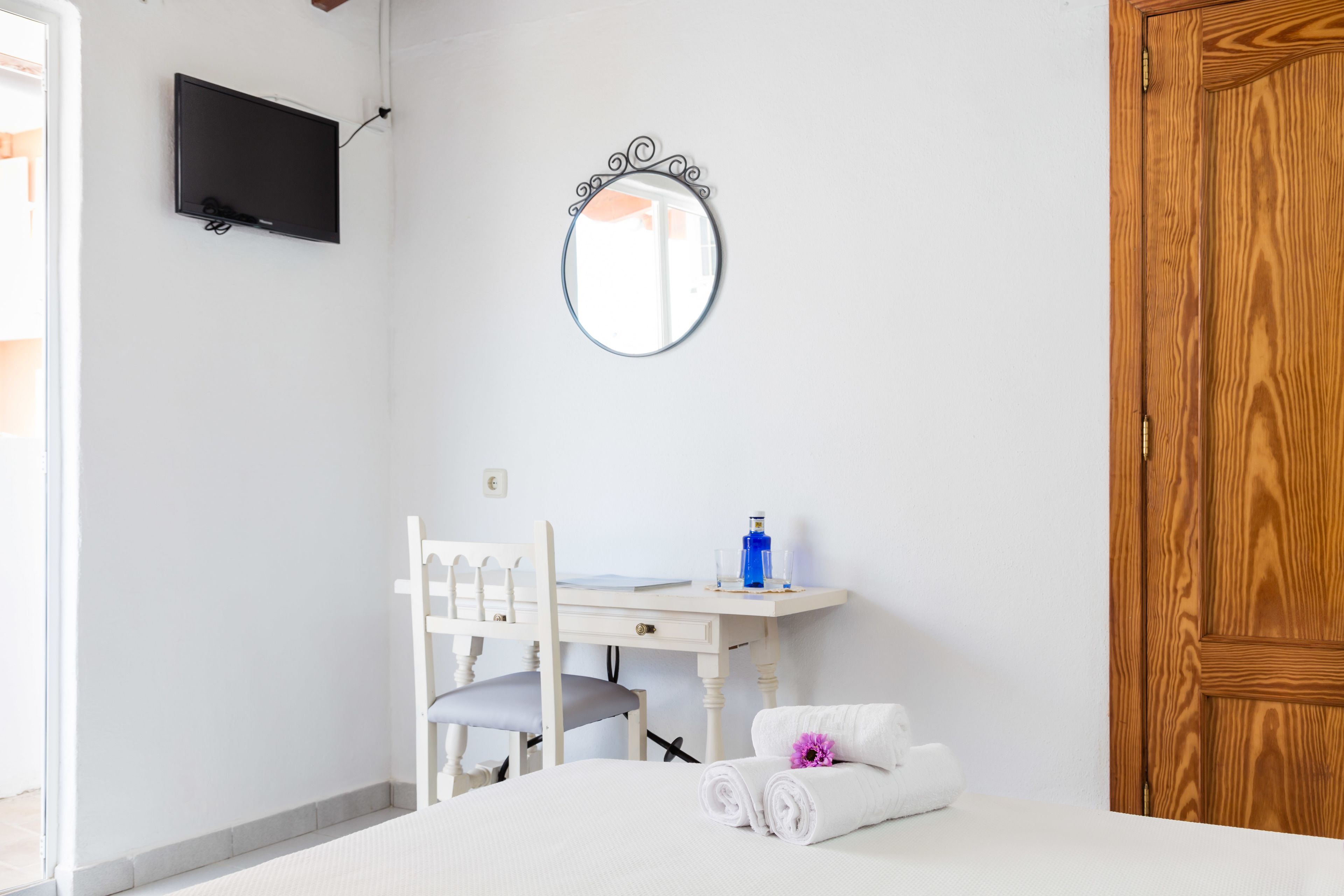 Un dormitorio con cama, escritorio, silla, televisor y puerta de madera.