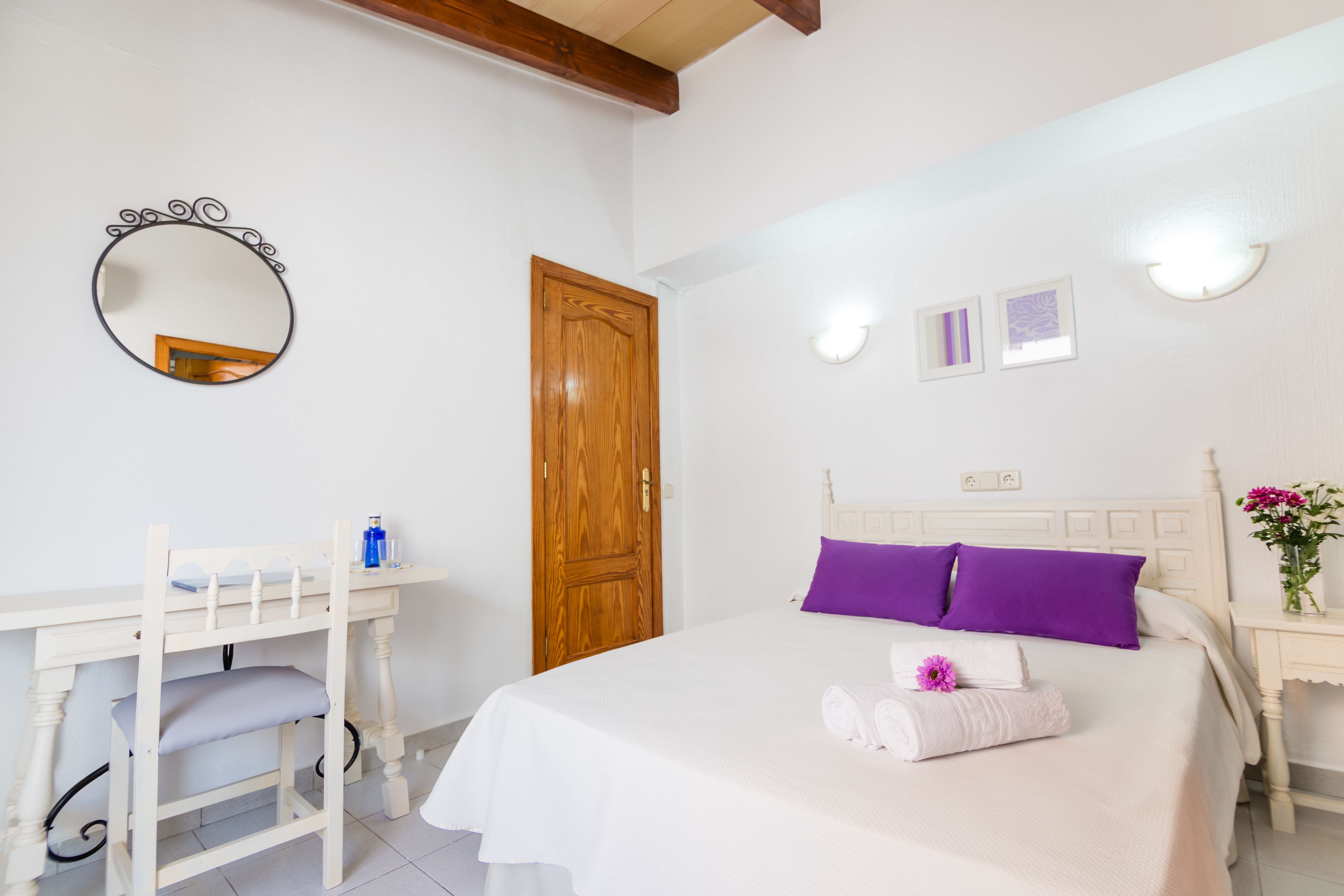 A bedroom with a bed, a desk, a mirror, and a door.