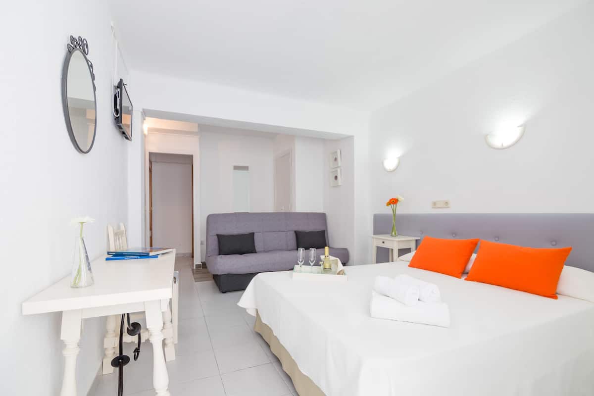 A hotel room with a bed, a sofa, a desk, and a mirror.