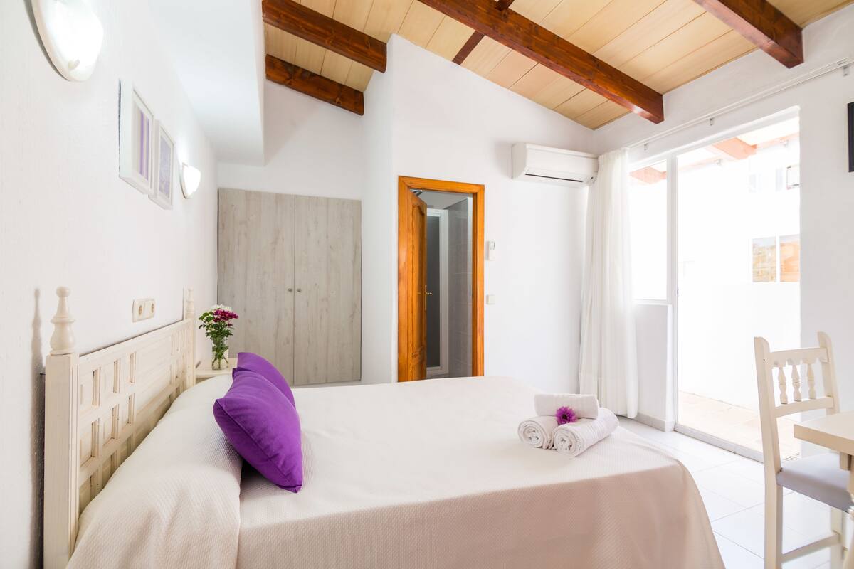 A bedroom with a bed, a wooden headboard, a small table with a towel, and a chair.