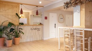 A hotel reception area with a wooden counter, potted plants, and a white door labeled "GARAU." - Garau Petit Hotel (Palma de Mallorca)