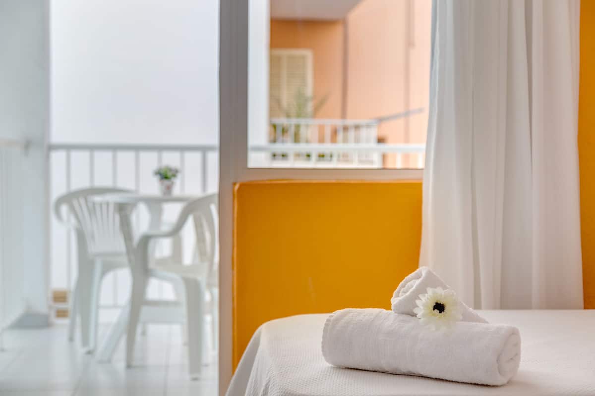 A neatly made bed with a white towel and a flower, a white chair, and a balcony with a railing.