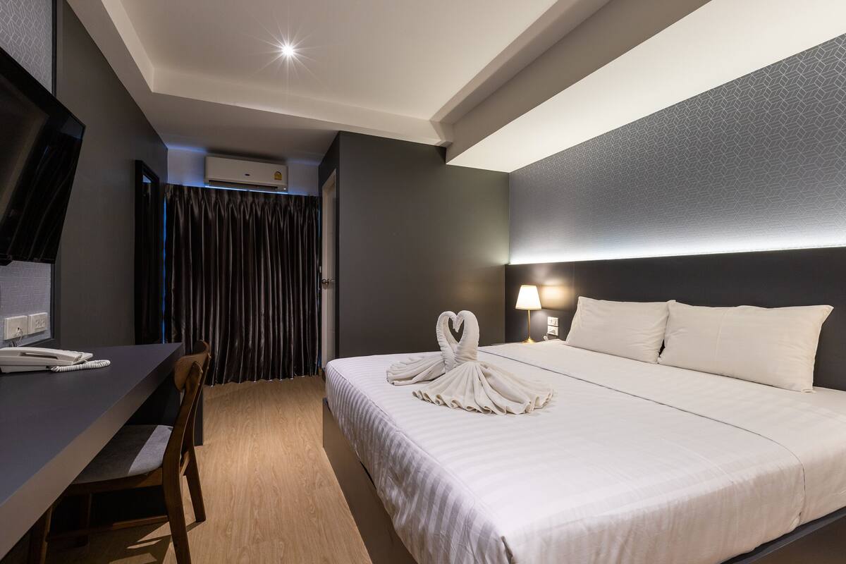 A hotel room with a bed, a desk, a chair, a lamp, and a curtain.