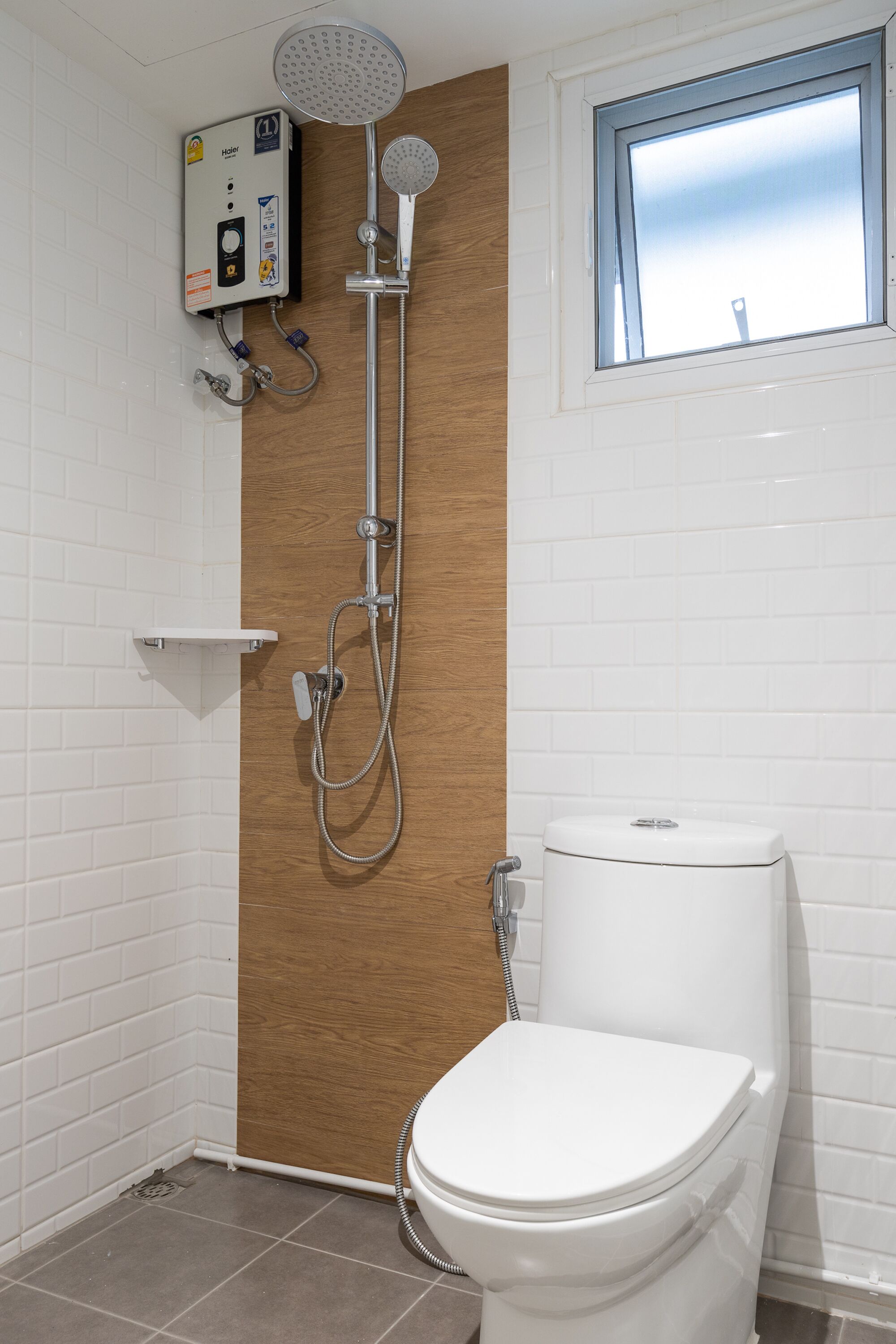 Une salle de bain avec des toilettes blanches, une douche avec un panneau en bois et une fenêtre.