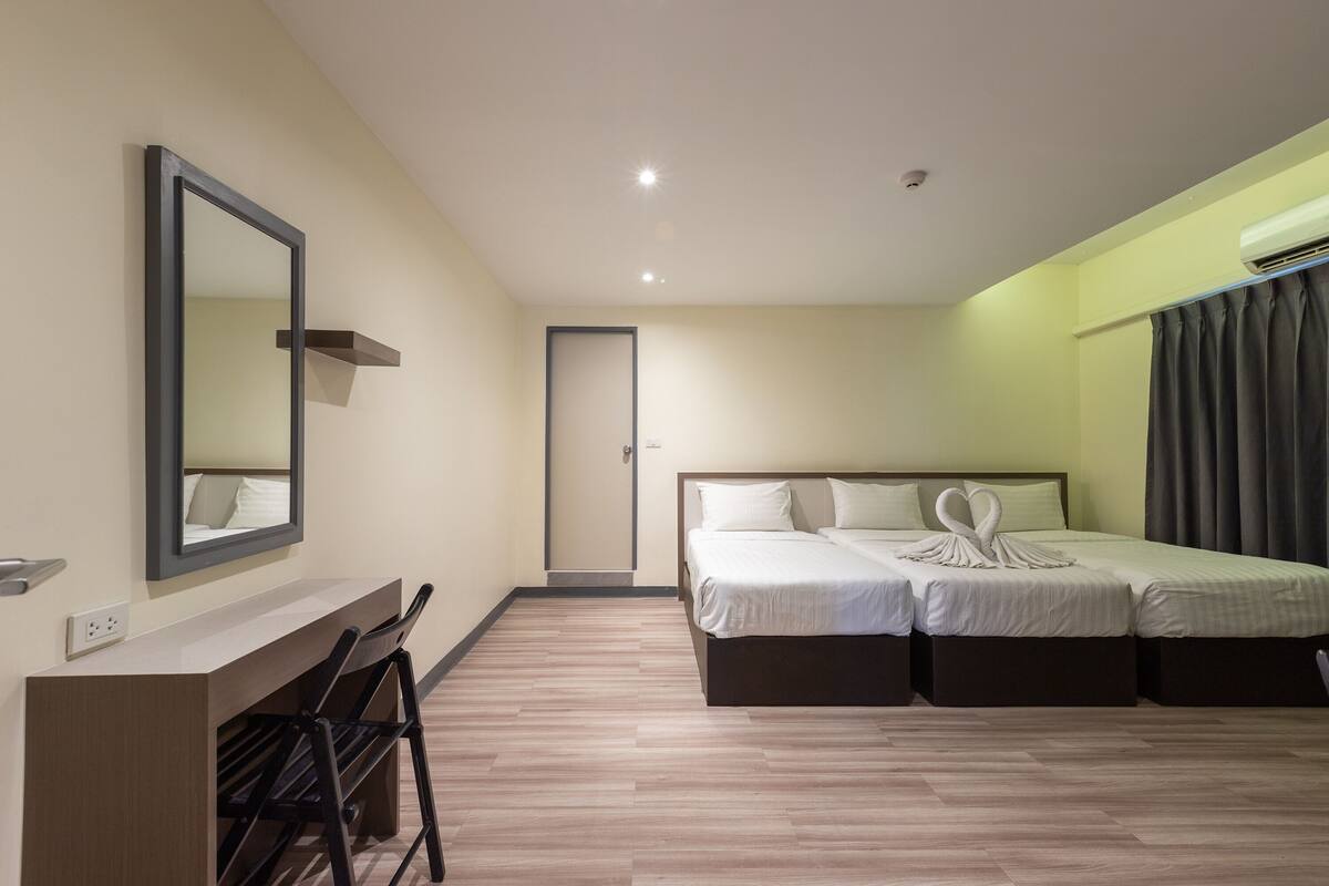 A hotel room with a desk, two beds, a mirror, and a door.