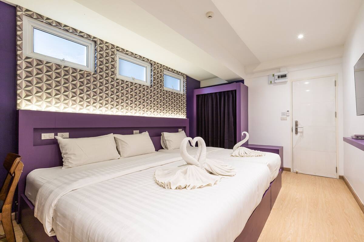 A hotel room with a large bed, two windows, a door, and a wall with geometric patterns.