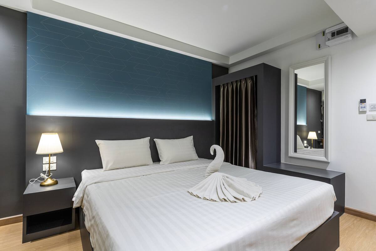 A modern hotel room with a large bed, a bedside table with a lamp, a mirror, and a geometric-patterned wall.