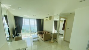 A modern living room with a sofa, a coffee table, and a TV. There is a balcony with a view of the sea. - The View Cosy Beach by PSR ASIA (Pattaya)