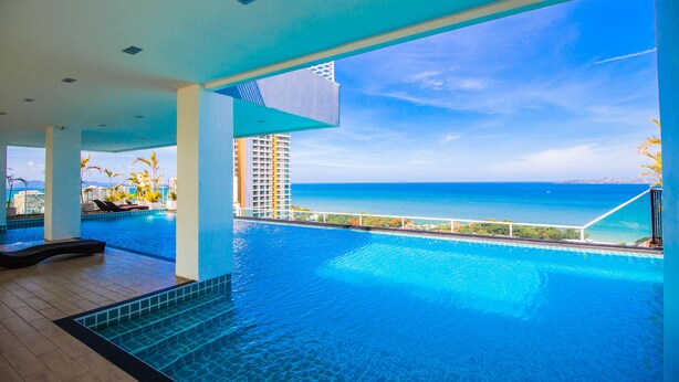 A large indoor swimming pool with a view of the ocean and a high-rise building in the background. - The View Cosy Beach by PSR ASIA (Pattaya)