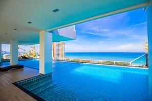 A large indoor swimming pool with a view of the ocean and a high-rise building in the background. - The View Cosy Beach by PSR ASIA (Pattaya)