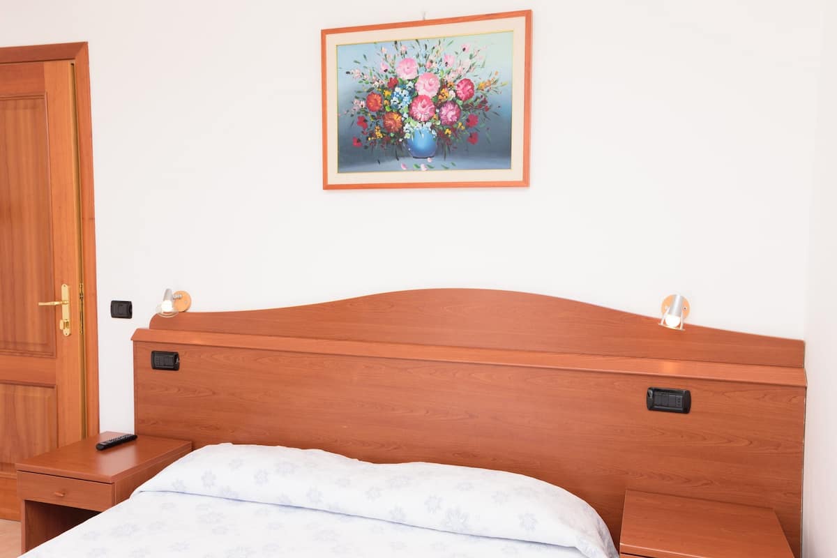 A bedroom with a wooden headboard, a bedside table with a lamp, and a framed floral painting on the wall.