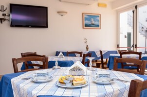 Un comedor con mesas dispuestas para el desayuno, con manteles a cuadros azules y blancos, sillas de madera y una variedad de productos para el desayuno, como pasteles y una tabla de quesos.