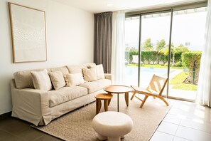 A modern living room with a sofa, round wooden tables, a chair, and a large window with a view of a garden.