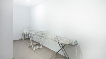 Una habitación con una tabla de planchar blanca y un tendedero blanco pegados a la pared.