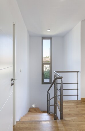 A modern staircase with wooden steps and a metal handrail, leading to a room with white walls and a window.