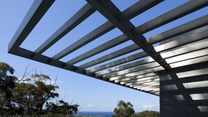 Una estructura arquitectònica moderna amb una sèrie de bigues horitzontals que creen un dibuix davant d'un cel blau clar.
