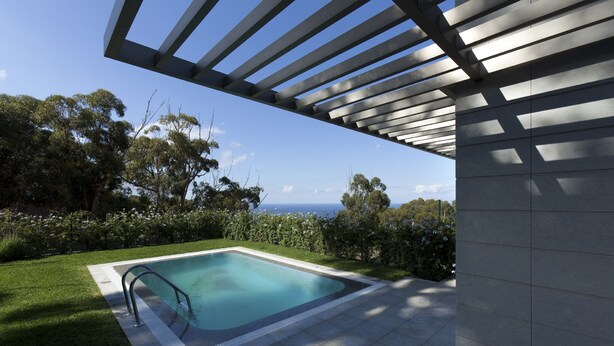 Zona de piscina exterior moderna amb una vista despejada de l'oceà, envoltada de vegetació exuberant i una estructura de pèrgola.