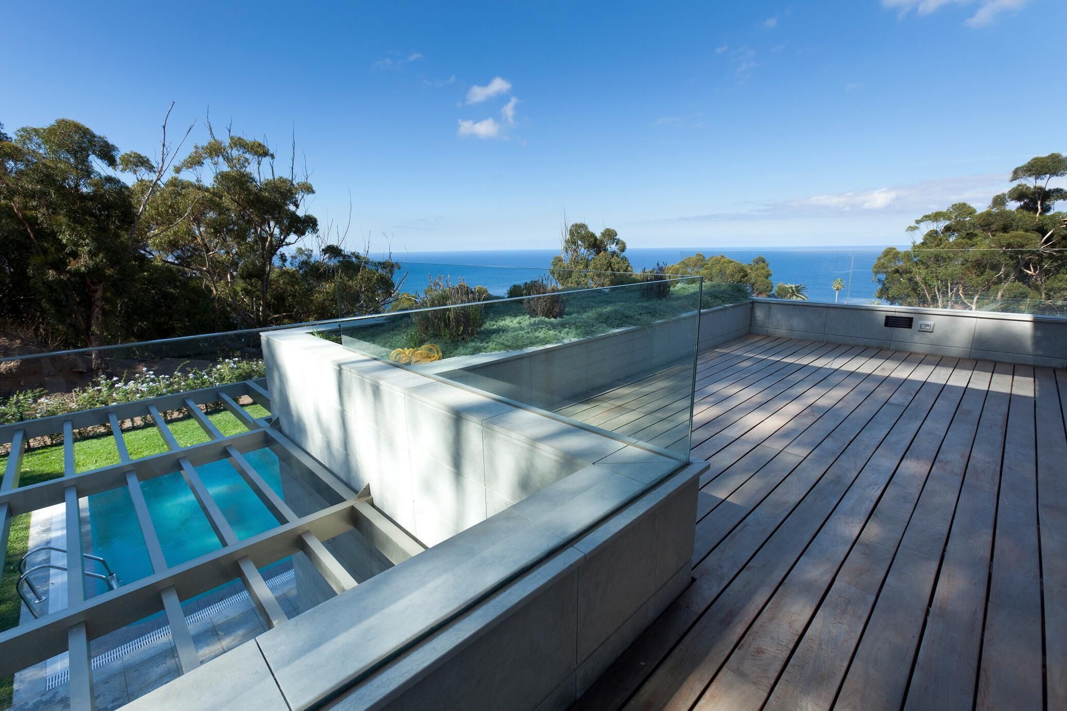 A rooftop deck with a swimming pool, a glass balustrade, and a view of the ocean.