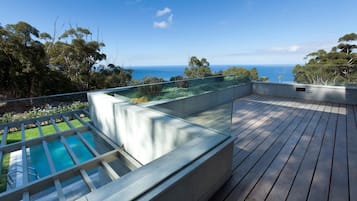 A rooftop deck with a swimming pool, a glass balustrade, and a view of the ocean.