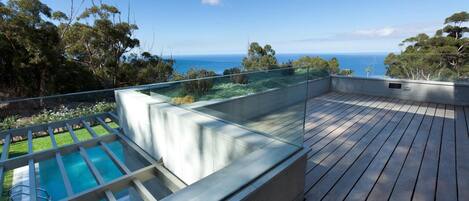 A rooftop deck with a swimming pool, a glass balustrade, and a view of the ocean.
