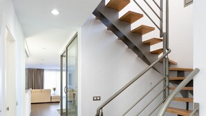 Una escala moderna amb graons de fusta i baranes metàl·liques que condueix a una zona d'estar amb un sofà i una finestra.
