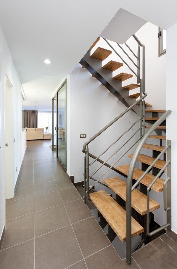 A modern staircase with wooden steps and metal railings, leading to a living area with a sofa and a window.