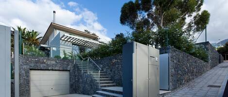 A modern building with a stone wall, a metal gate, and a staircase leading to a garage.