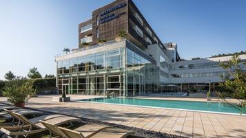 A modern hotel with a glass facade, outdoor pool, and lounge chairs.