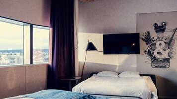 Quarto de hotel com duas camas, uma janela ampla com vista, uma TV de tela plana e uma obra de arte na parede.