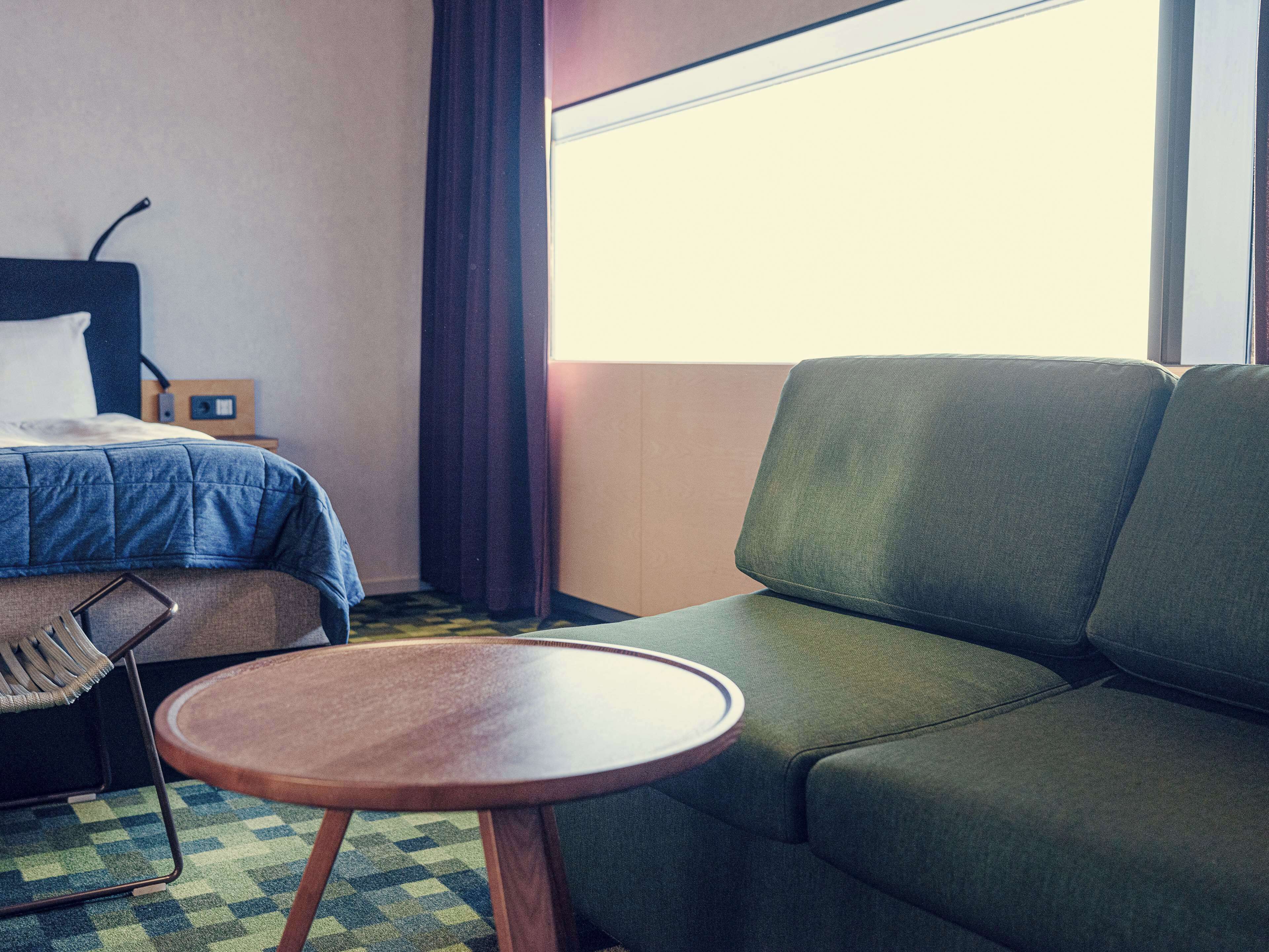 A hotel room with a bed, a green sofa, a small wooden table, and a checkered floor.