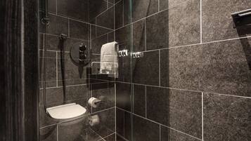 A modern bathroom with dark tiles, a glass shower enclosure, a toilet, and a towel rack.