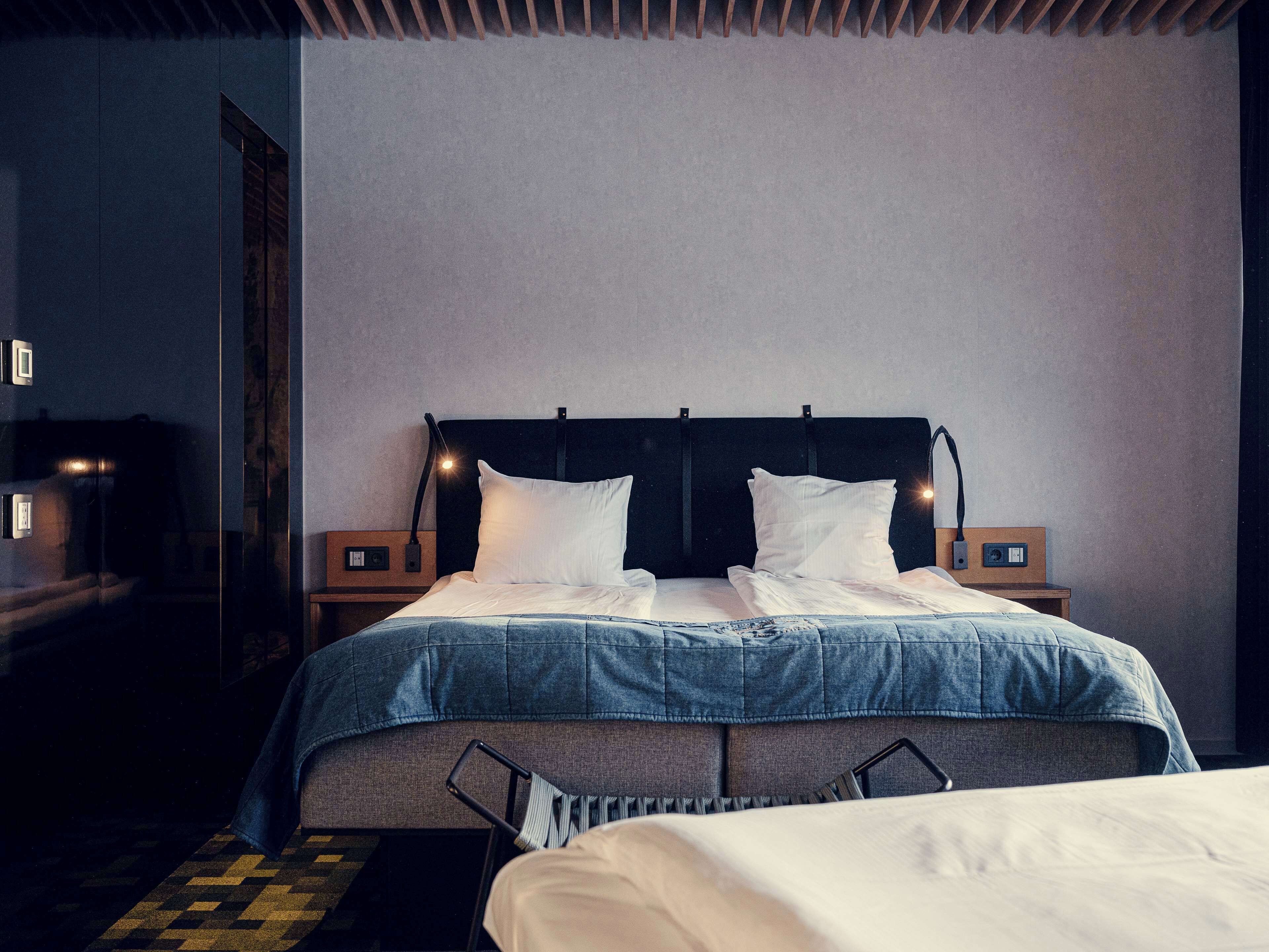 A neatly made bed with a denim cover, a headboard with integrated reading lights, and bedside tables with lamps.
