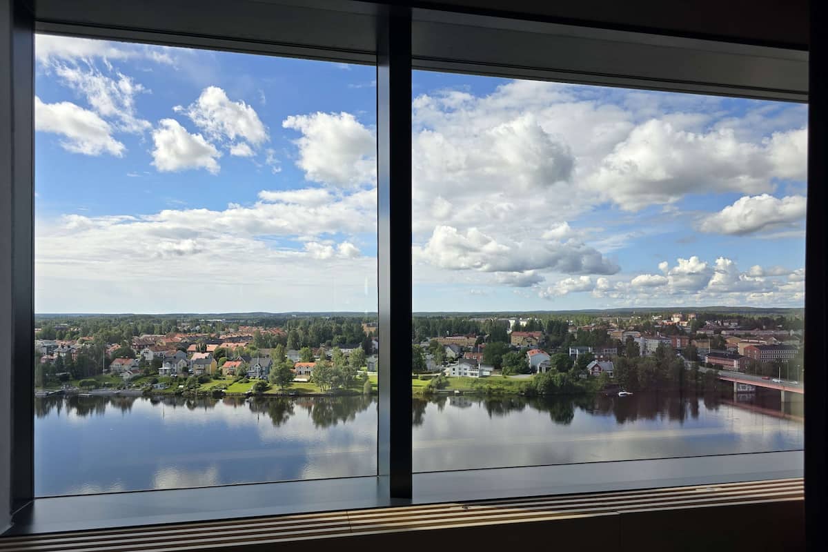 A view from a window overlooking a lake with a town in the distance, a bridge, and a partly cloudy sky.