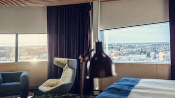 Ein Hotelzimmer mit großem Fenster, einem Bett, einem Sessel und einer Lampe.