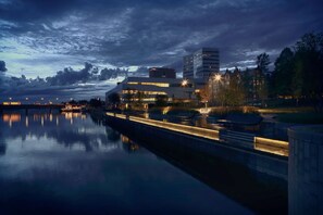 A waterfront hotel with a modern design, featuring a reflective pool and a view of the city skyline.