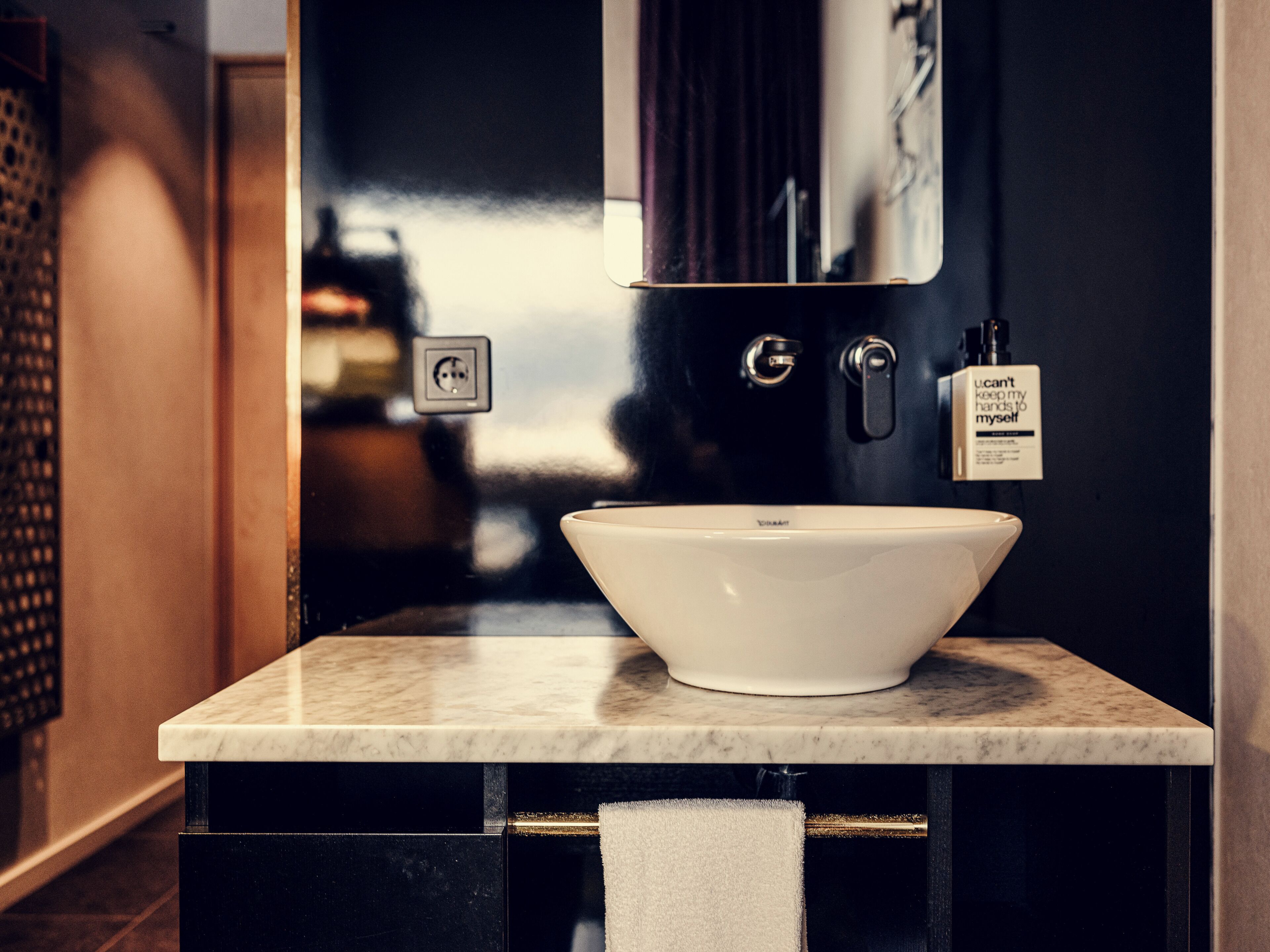 A bathroom with a white sink, a mirror, a towel rack, and a soap dispenser.